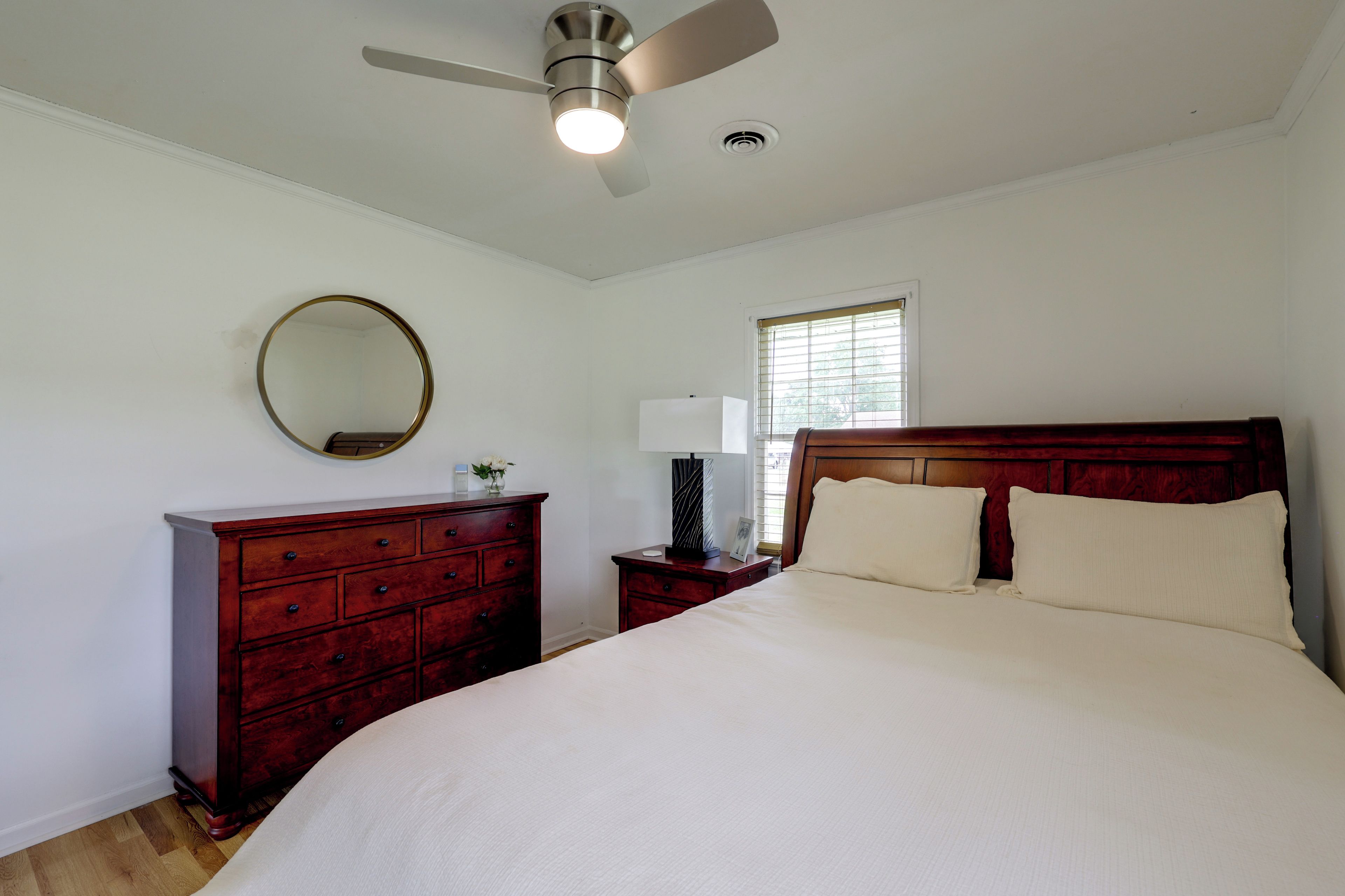 A bedroom with a bed, a dresser, a nightstand, a mirror, a ceiling fan, and a window.