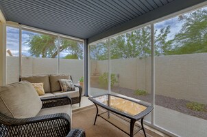 A covered patio area with a sofa and a table, large windows, and a view of trees.