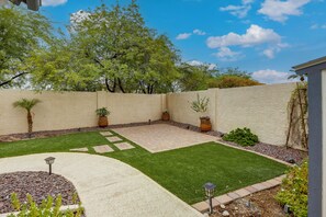 A landscaped backyard with a paved patio, a lawn, and a variety of potted plants. - Near Golf & Outdoor Fun! West Valley Retreat (Peoria)