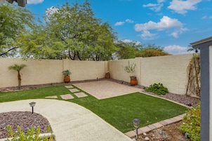 Un jardín ajardinado con un patio empedrado, césped y una variedad de plantas en macetas.