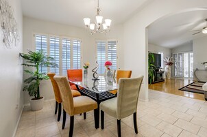 A dining area with a glass table surrounded by chairs, a chandelier, and a potted plant.