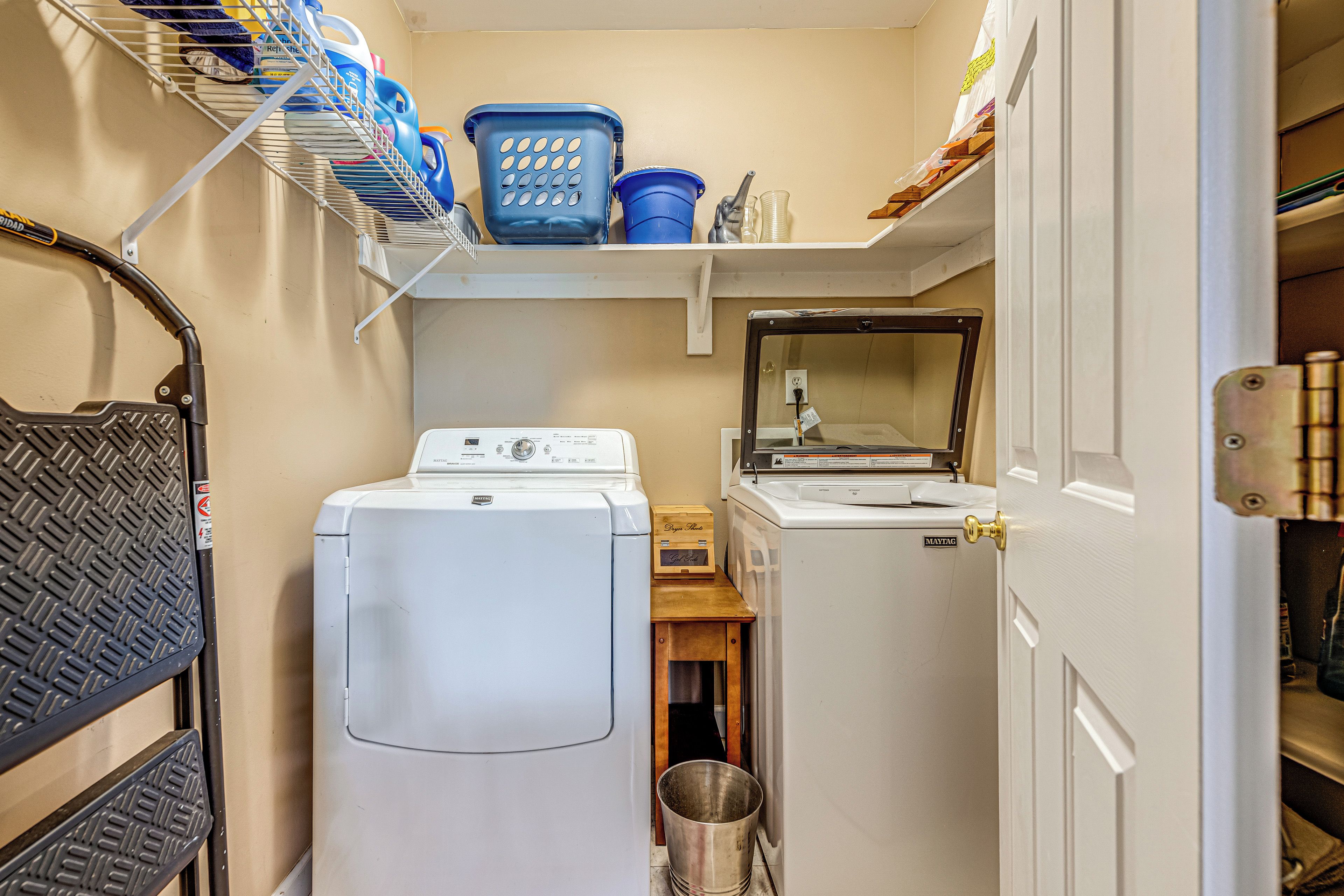 Une petite buanderie équipée d’un lave-linge et d’un sèche-linge à chargement frontal, d’un étendoir métallique et d’une étagère contenant le nécessaire pour faire la lessive.