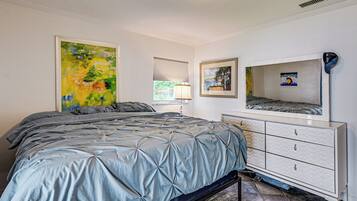 Un dormitorio con una cama, un aparador, una ventana con persianas y dos cuadros en la pared.