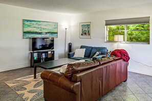 Een woonkamer met een bruine leren bank, een flatscreen televisie, een salontafel en kunstwerken aan de muur.
