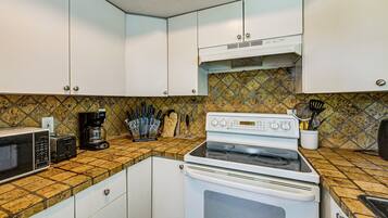 A kitchen with white cabinets, a stove, a microwave, and a coffee maker.