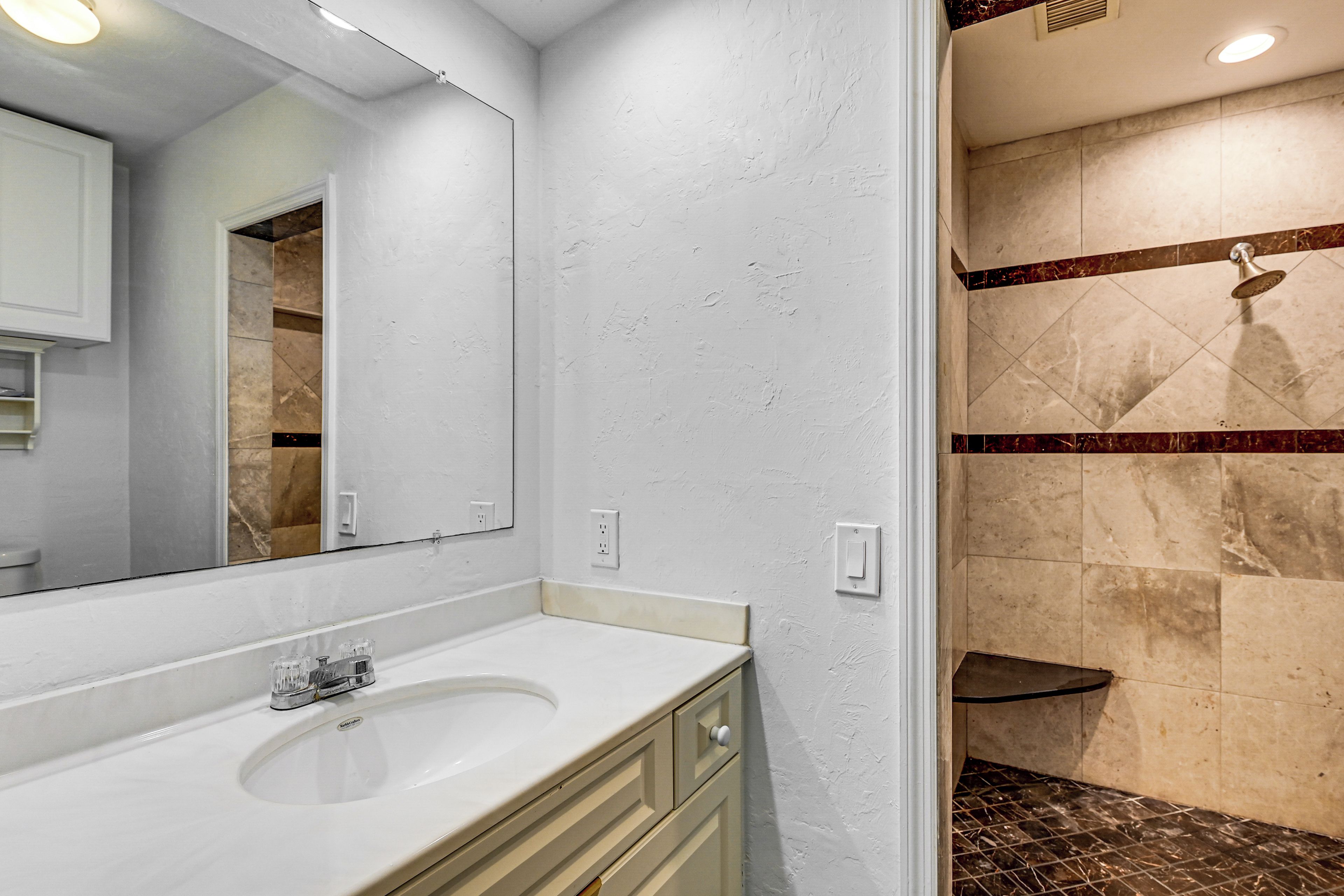 Un baño con lavamanos blanco, espejo y zona de ducha con paredes de azulejos.