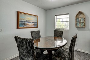 A dining area with a round table and woven chairs, a painting on the wall, a window with a view, and a decorative arched mirror. - Yard & Patio! Naples Home By Botanical Garden (Naples)