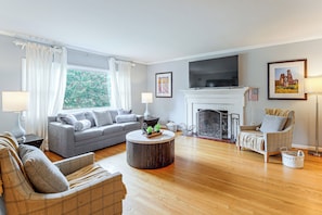 A living room with a fireplace, a sofa, a chair, a television, and a window with curtains.