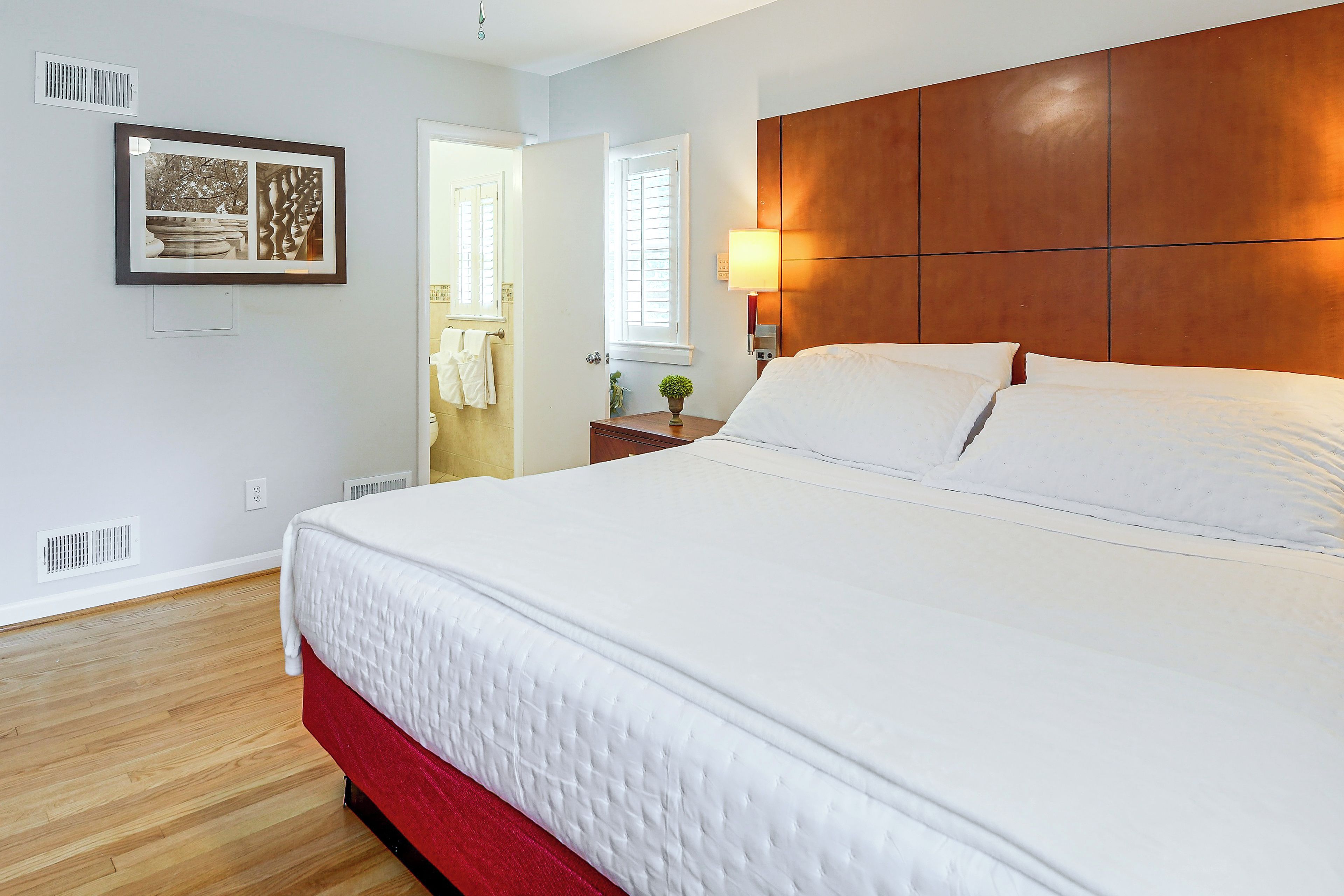 A hotel room with a large bed, a wooden headboard, a bedside table with a lamp, and a framed picture on the wall.