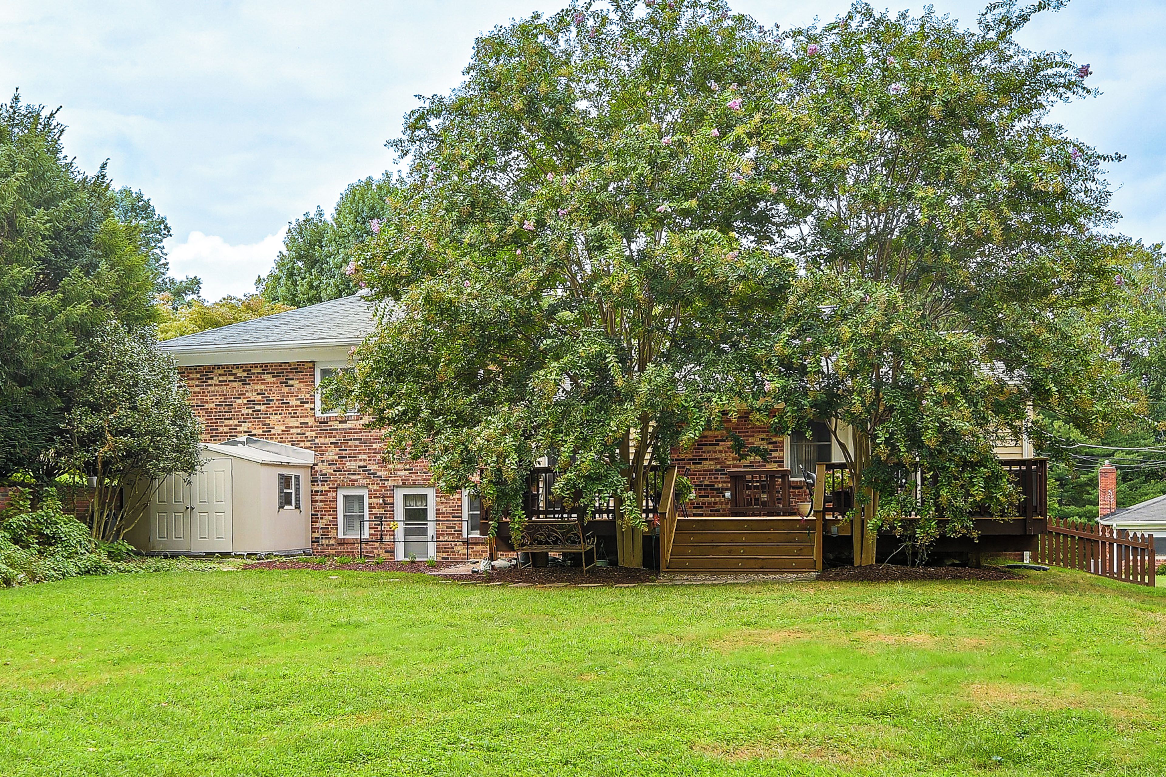 A brick house with a garage, a wooden deck, and a well-maintained lawn.