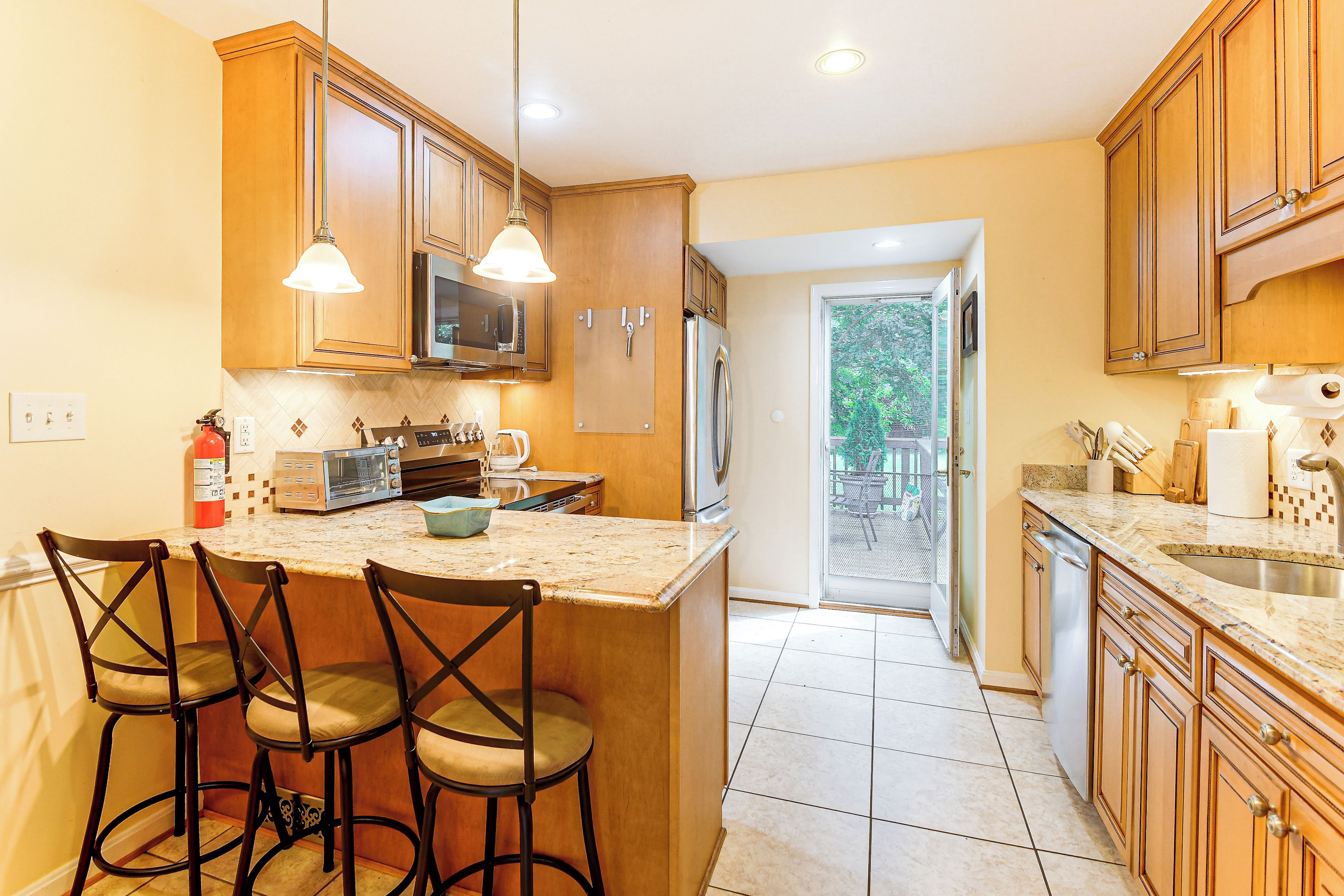 A kitchen with wooden cabinets, a built-in microwave, a refrigerator, and a bar area with stools.