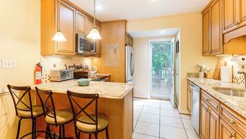 A kitchen with wooden cabinets, a built-in microwave, a refrigerator, and a bar area with stools.