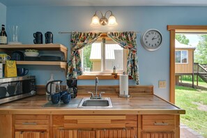 A kitchen with wooden cabinets, a sink, and a window with curtains. There is a clock on the wall and a wooden deck outside. - Hike, Fish & Unwind! Catskills Studio w/ Mtn Views (Hobart)
