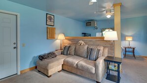 A room with a beige sectional sofa, a small table, a ceiling fan, and a wooden headboard. - Hike, Fish & Unwind! Catskills Studio w/ Mtn Views (Hobart)