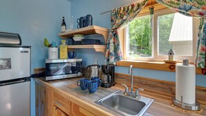 A compact kitchen with a refrigerator, microwave, coffee maker, and a sink. There are wooden shelves above the counter holding dishes and a birdhouse on the window sill. - Hike, Fish & Unwind! Catskills Studio w/ Mtn Views (Hobart)