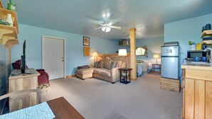 A cozy living room with a sofa, a dining table, and a kitchen area with a refrigerator and cabinets. - Hike, Fish & Unwind! Catskills Studio w/ Mtn Views (Hobart)