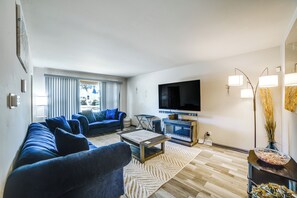 En moderne stue med et stort fladskærms-TV, blå sofaer, et sofabord og en gulvtæppe med mønster.
