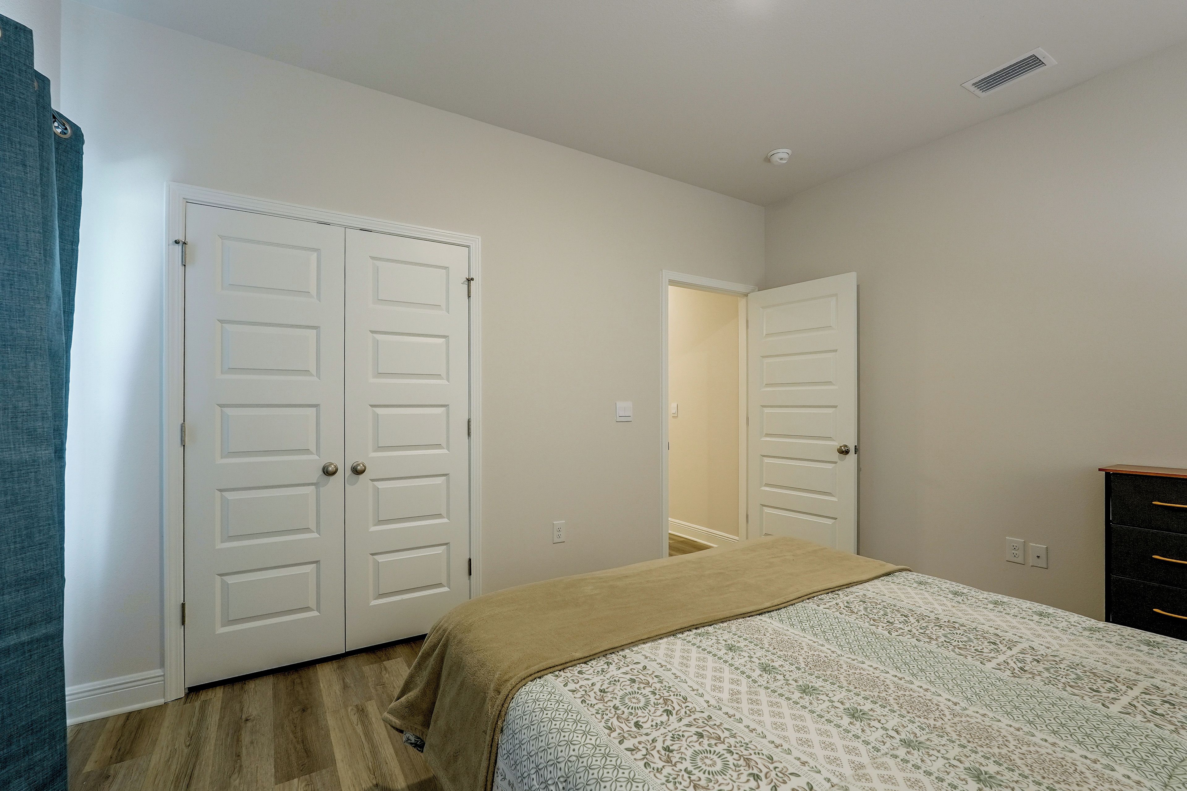 Quarto com cama, cômoda e duas portas brancas.