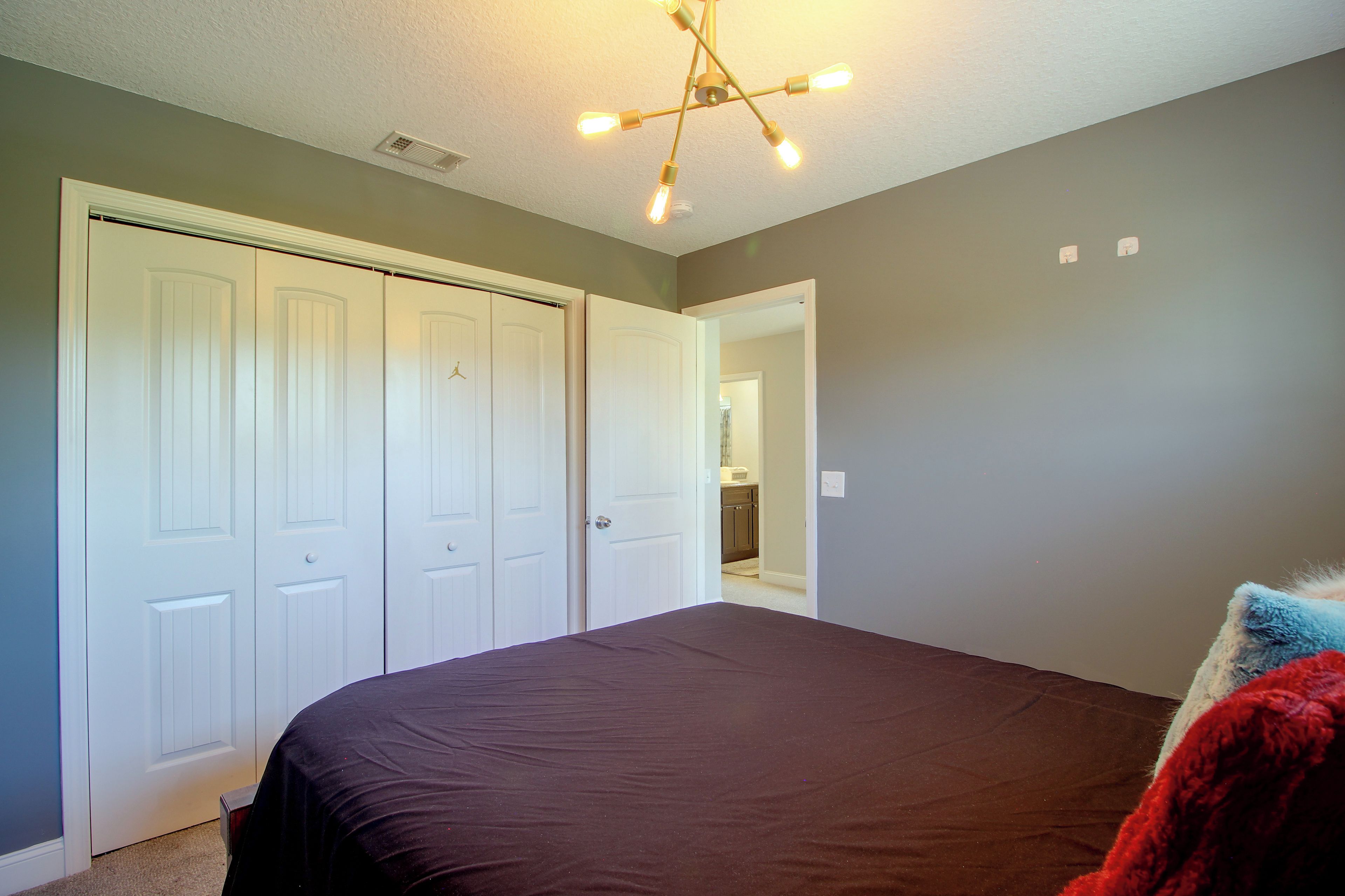 A bedroom with a large bed, a closet with white doors, and a ceiling light fixture.