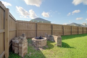A backyard with a wooden fence, a brick fire pit, and a grassy lawn.