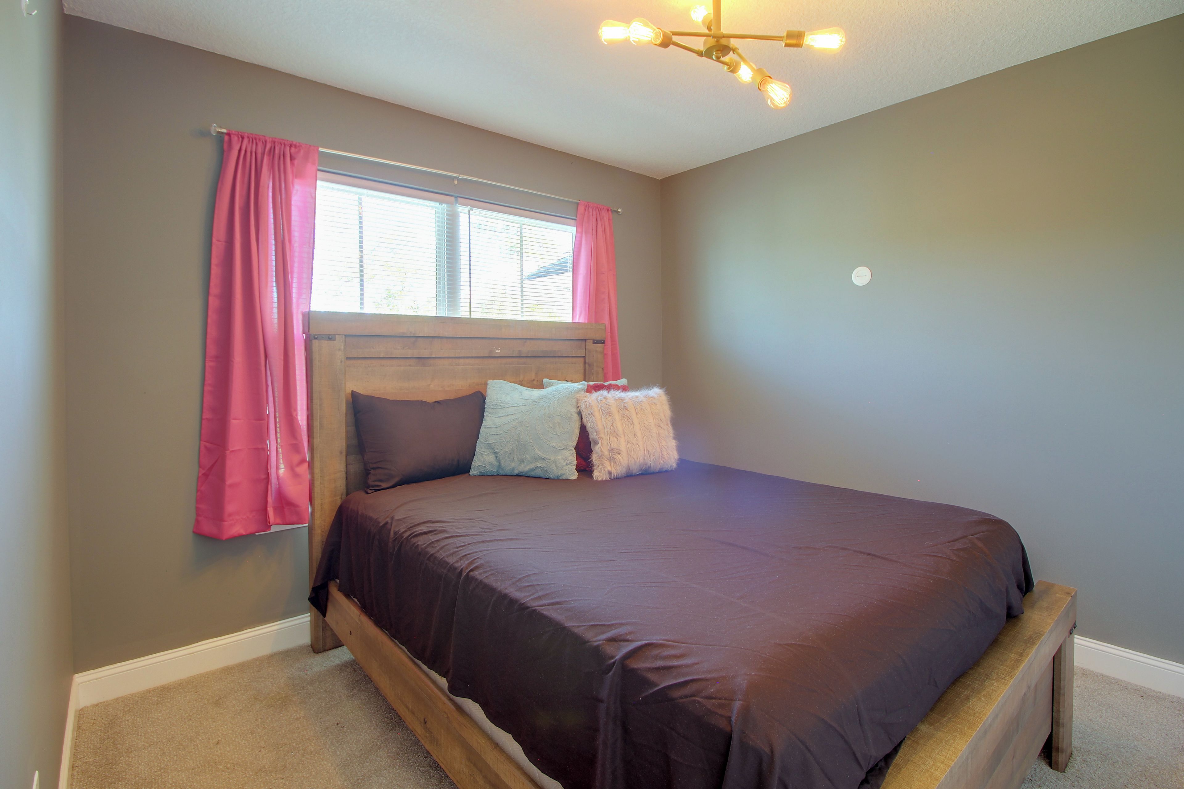 A bedroom with a bed, a window with curtains, and a ceiling light fixture.