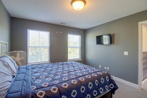 A bedroom with a bed, two windows, a ceiling fan, and a mounted TV.