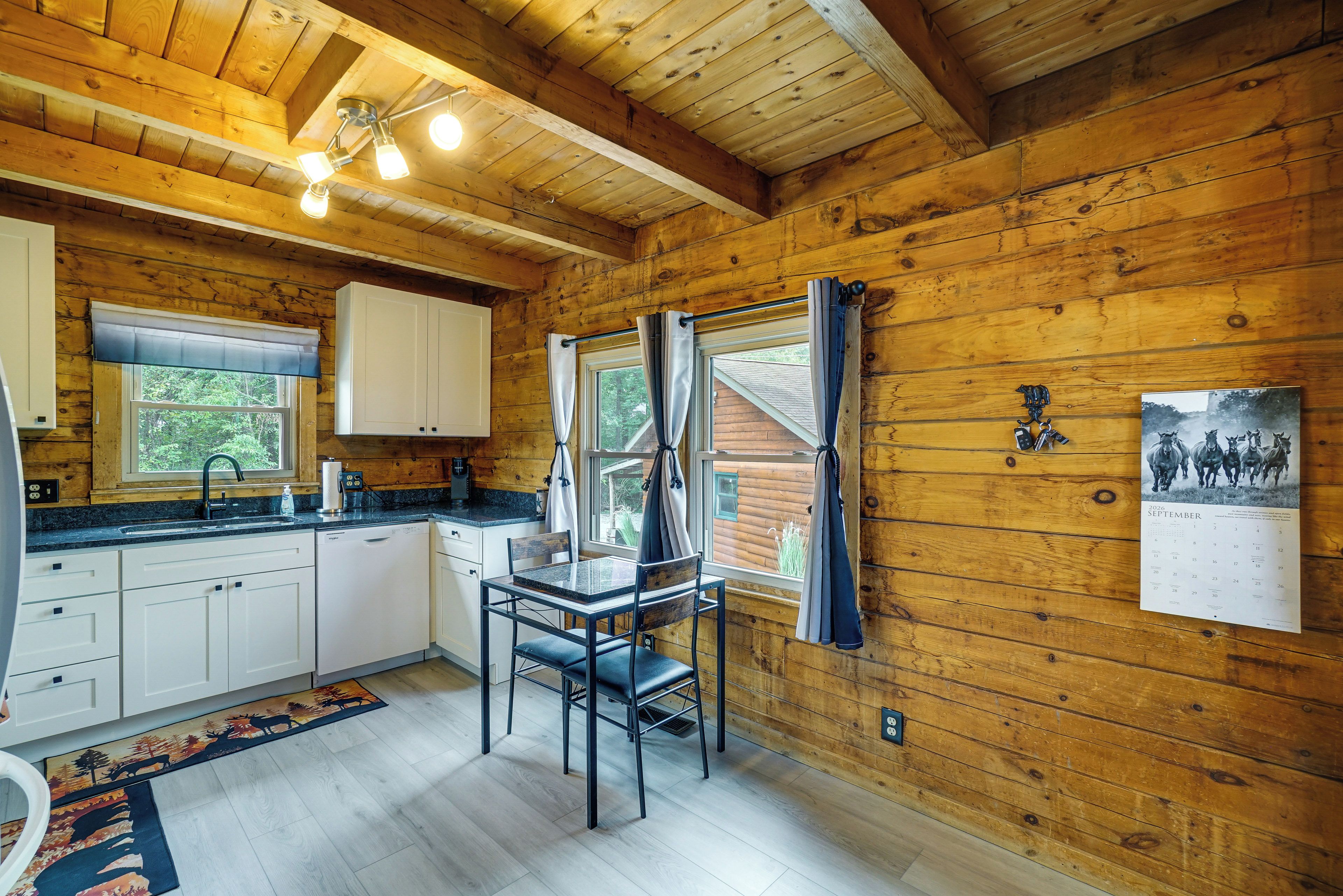 A wooden cabin interior with a kitchen, dining area, and a calendar on the wall.