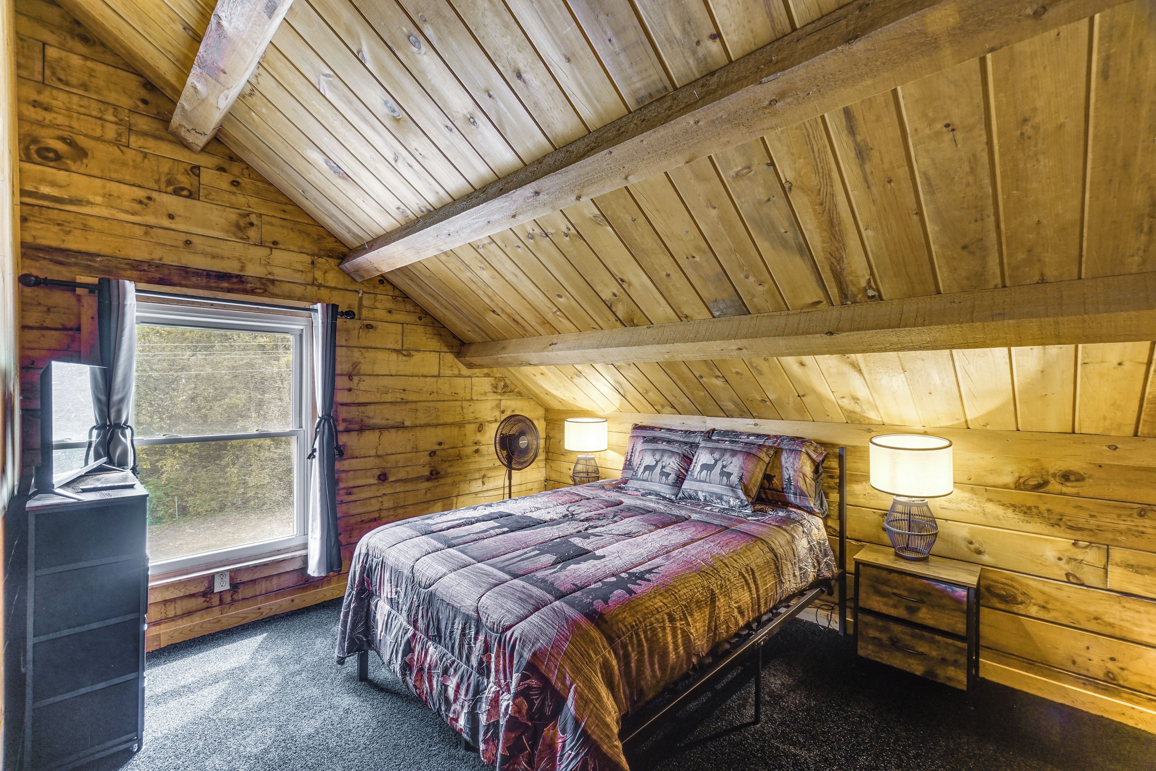 A cozy room with a sloped ceiling, a bed with patterned bedding, bedside lamps, and a window with curtains.