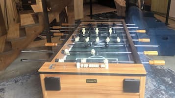 A foosball table with a wooden base and black accents, located in a room with a concrete floor and wooden furniture.