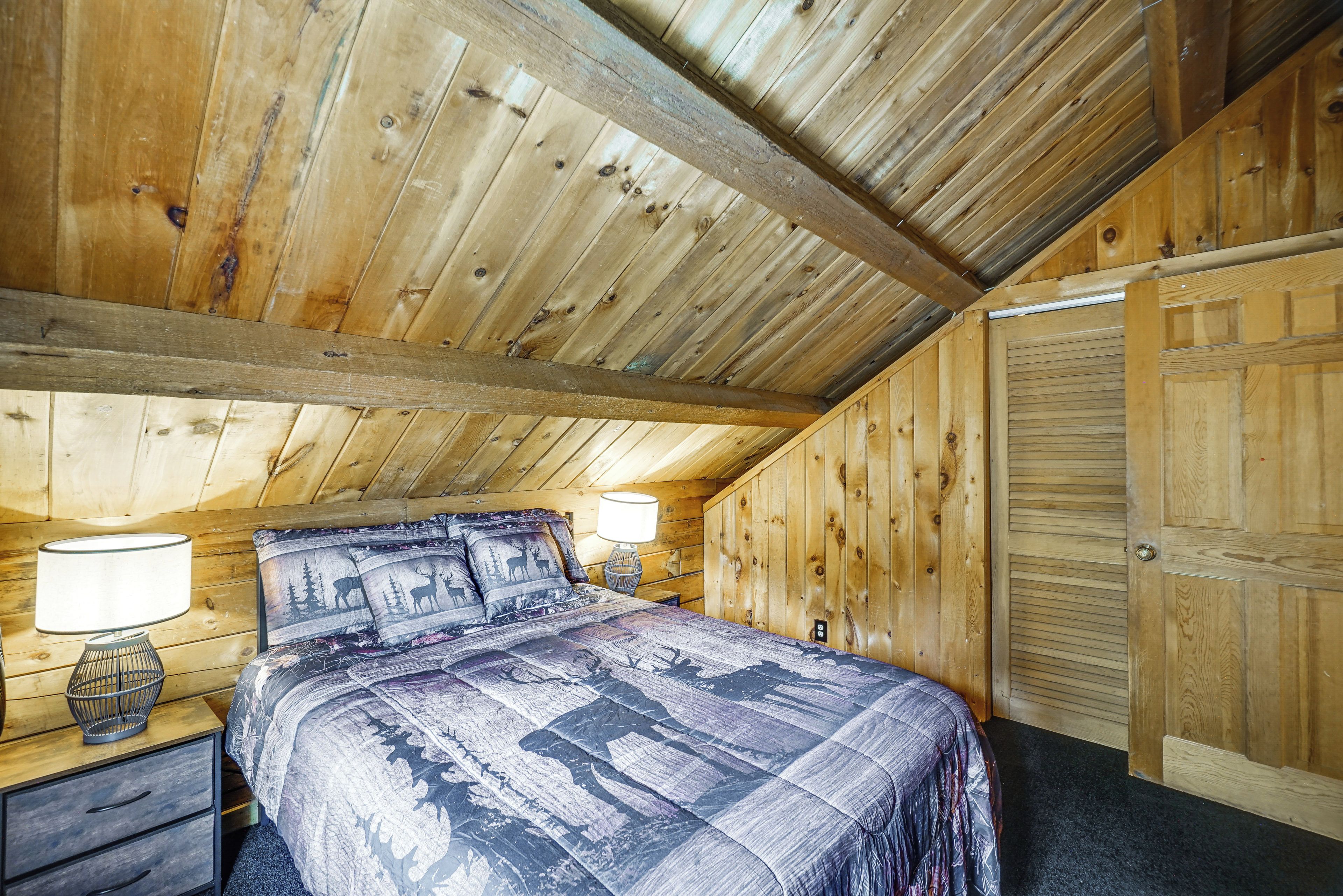 A bedroom with a wooden ceiling, a bed with patterned bedding, two bedside lamps, and a nightstand with a basket.