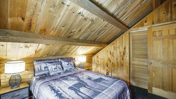 A bedroom with a wooden ceiling, a bed with patterned bedding, two bedside lamps, and a nightstand with a basket.