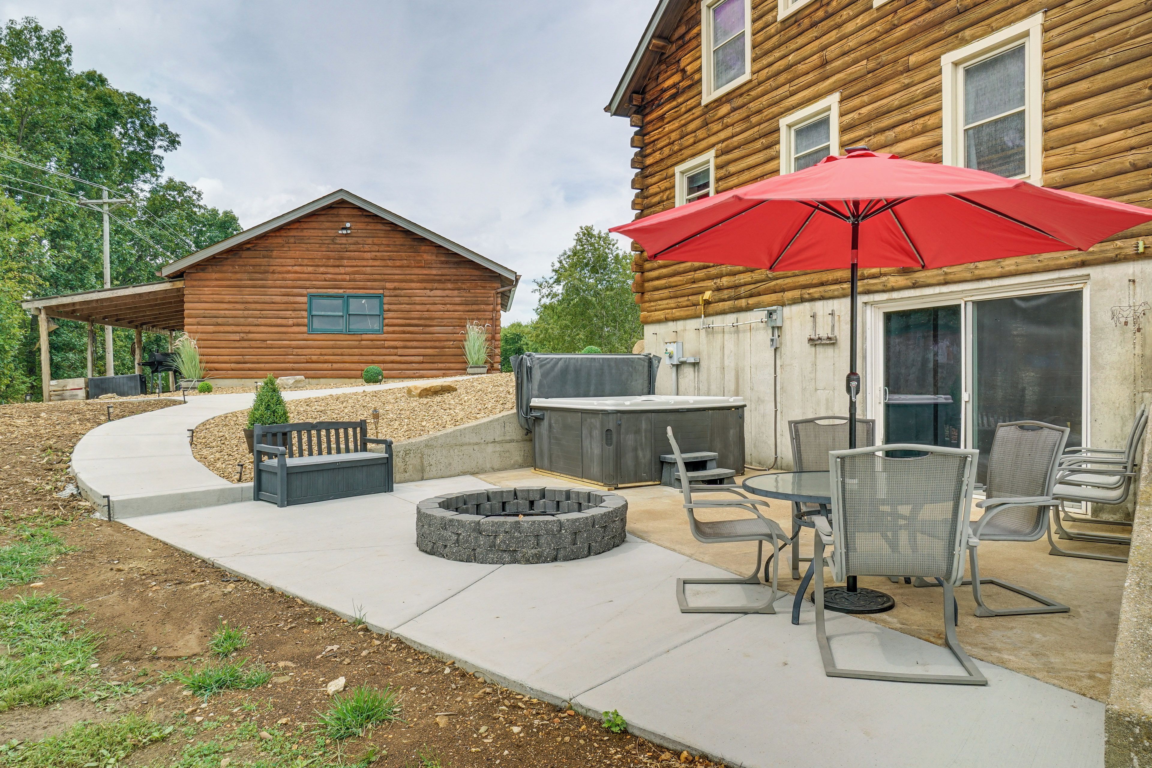 A wooden cabin with a patio area featuring a hot tub, seating, and a red umbrella.