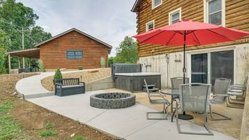 A wooden cabin with a patio area featuring a hot tub, seating, and a red umbrella.