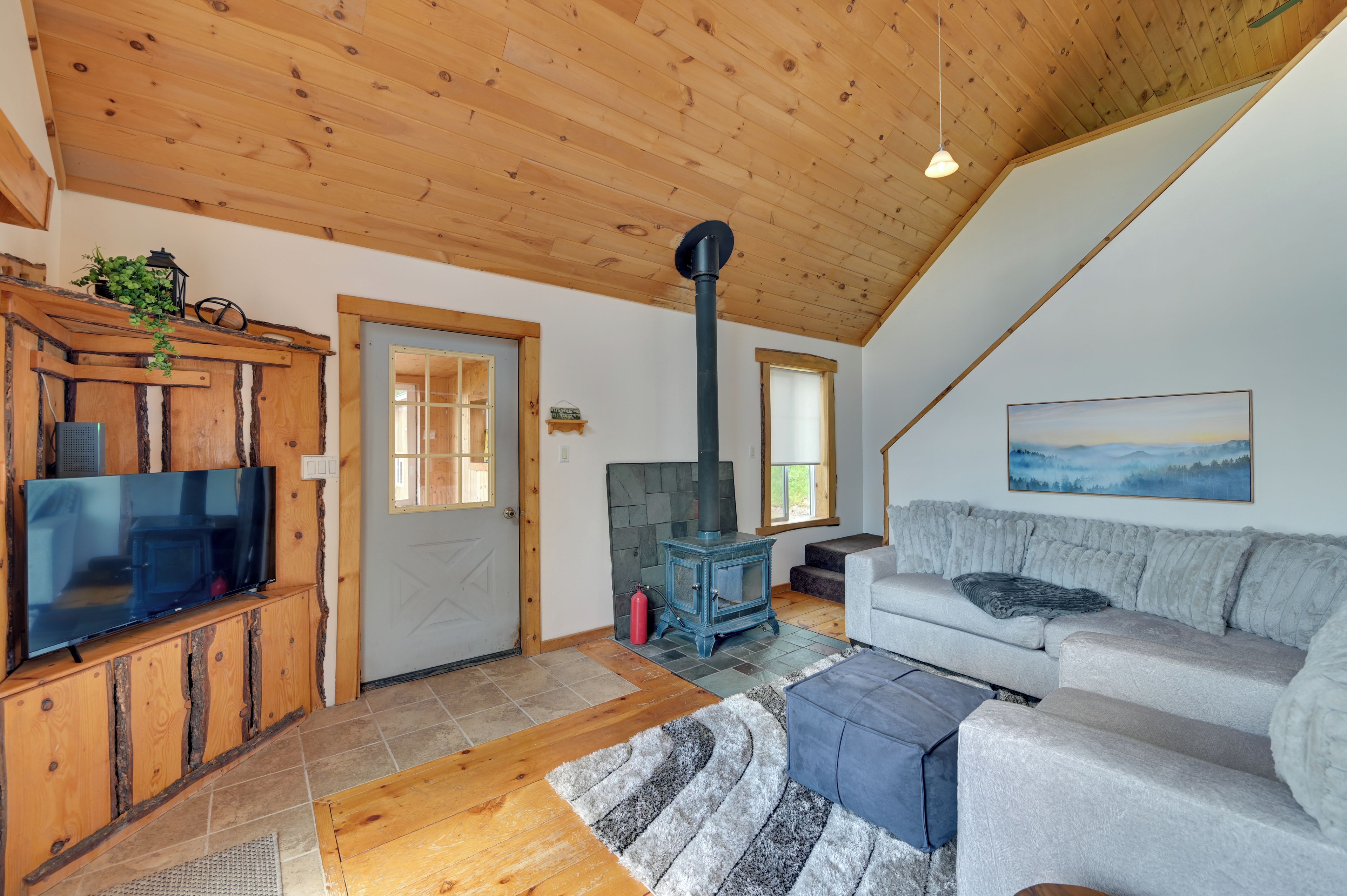 A cozy living room with a wooden ceiling, a television on a wooden cabinet, a sofa, a rug, and a fireplace.