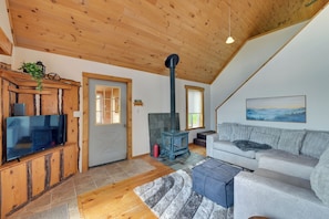 A cozy living room with a wooden ceiling, a television on a wooden cabinet, a sofa, a rug, and a fireplace.