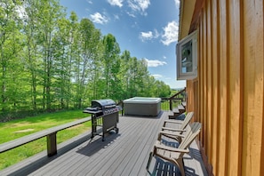 Een houten terras met een barbecue, jacuzzi en lounge stoelen.