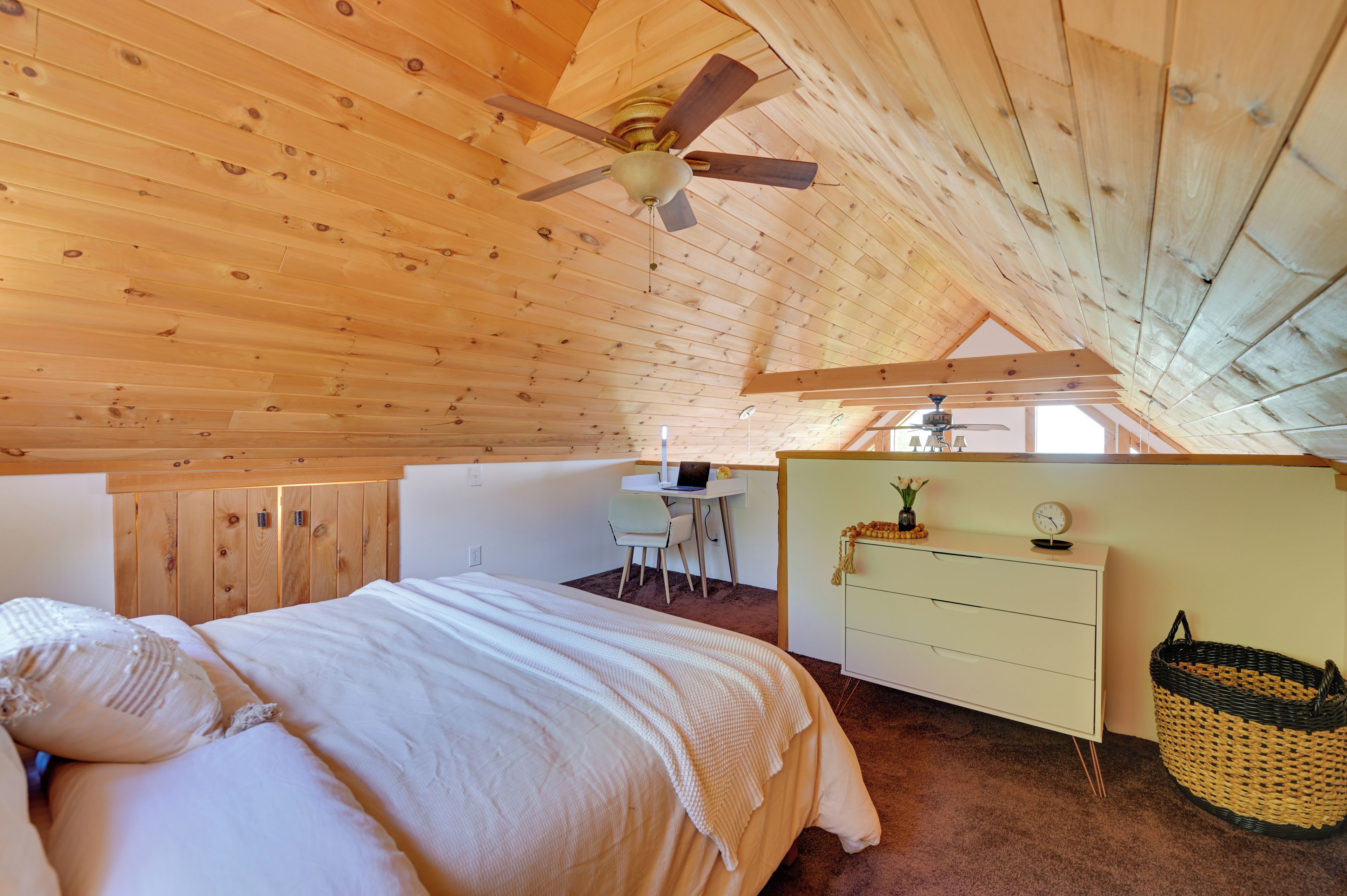 A bedroom with a wooden ceiling, a bed, a desk, and a dresser.