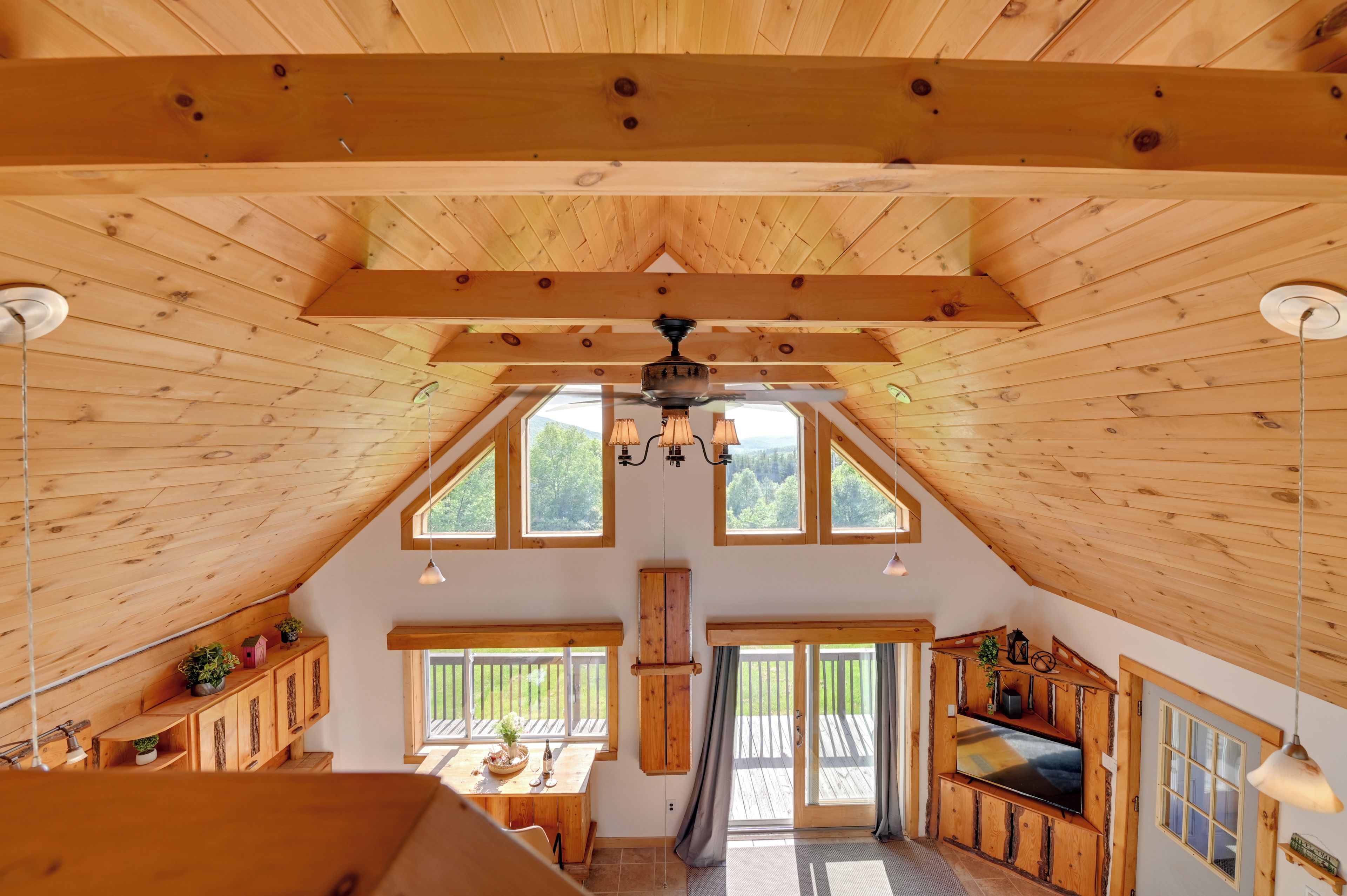 A spacious attic room with wooden beams, large windows, a ceiling fan, and a cozy seating area.