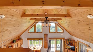 A spacious attic room with wooden beams, large windows, a ceiling fan, and a cozy seating area.