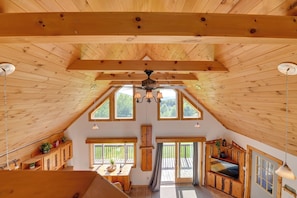 A spacious attic room with wooden beams, large windows, a ceiling fan, and a cozy seating area. - Hot Tub & Amazing Views! Family Catskills Cabin (Hobart)