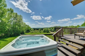 A hot tub on a wooden deck with a view of a green landscape and trees.
