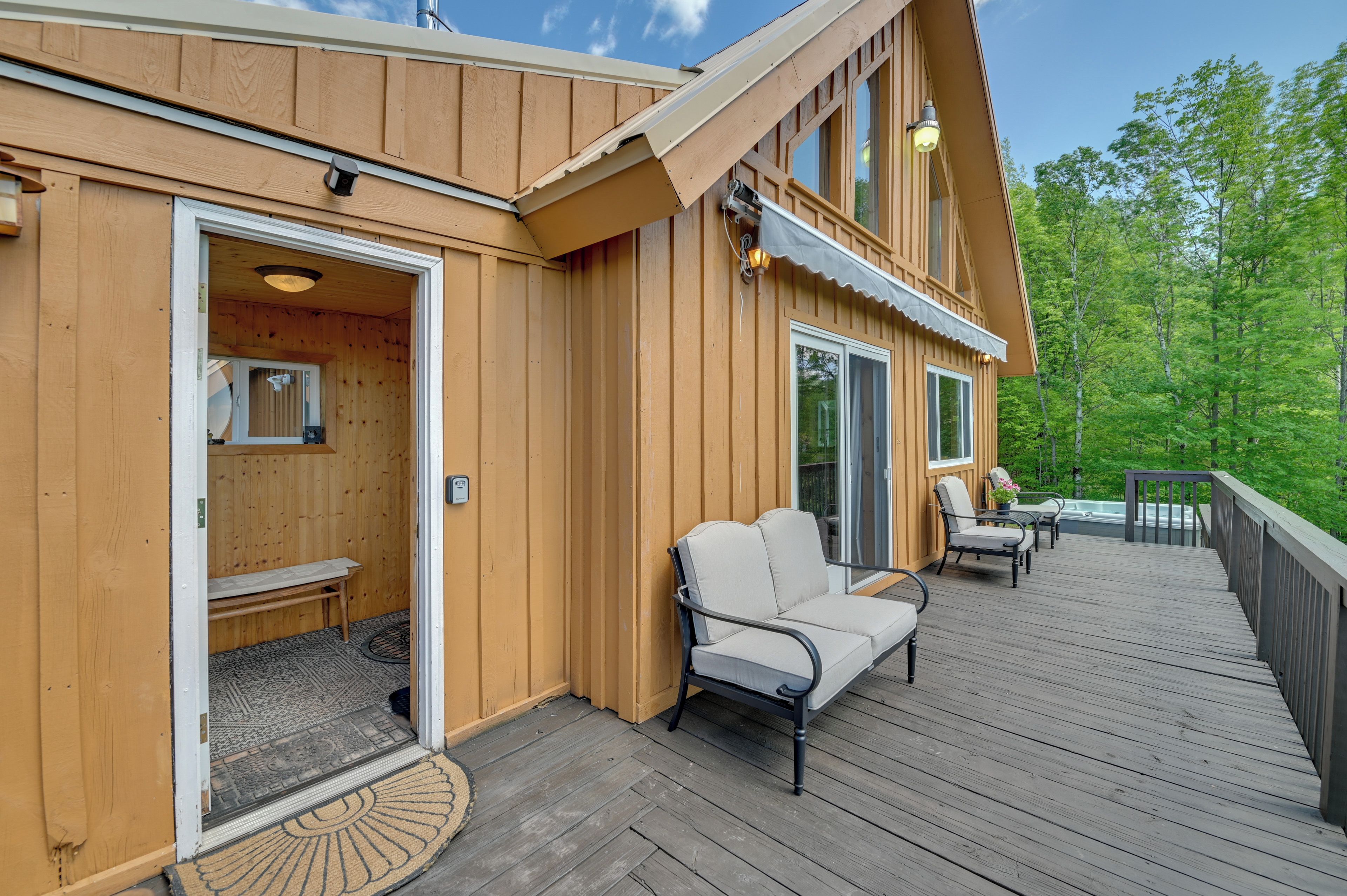 Una baita di legno con una veranda, una zona salotto esterna coperta e una porta che dà su un ambiente interno.
