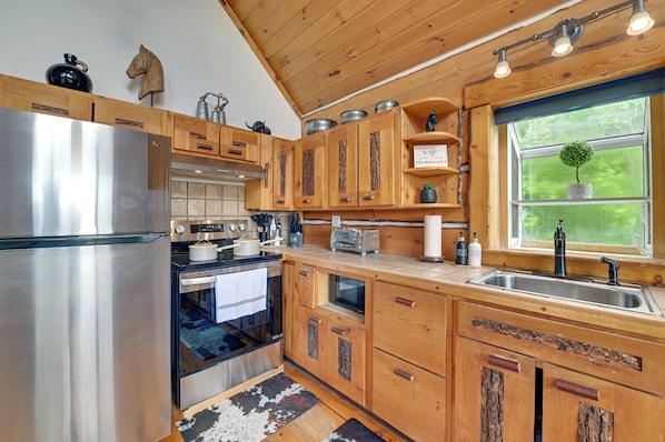 A kitchen with wooden cabinets, stainless steel appliances, and a window with a view of greenery.