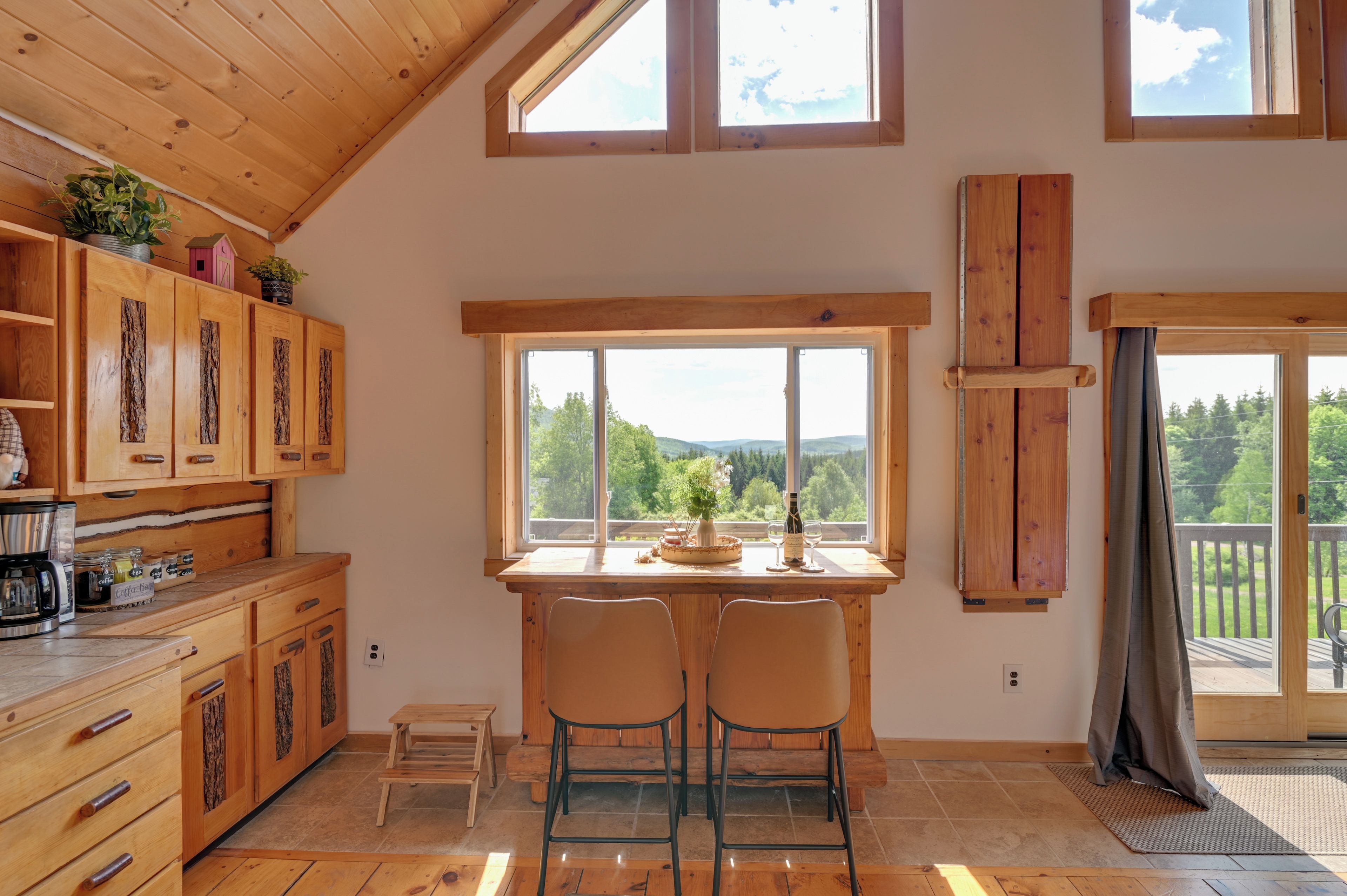 A cozy kitchen with wooden cabinets, a dining area with two chairs, and large windows offering a view of the outdoors.