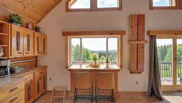 A cozy kitchen with wooden cabinets, a dining area with two chairs, and large windows offering a view of the outdoors.