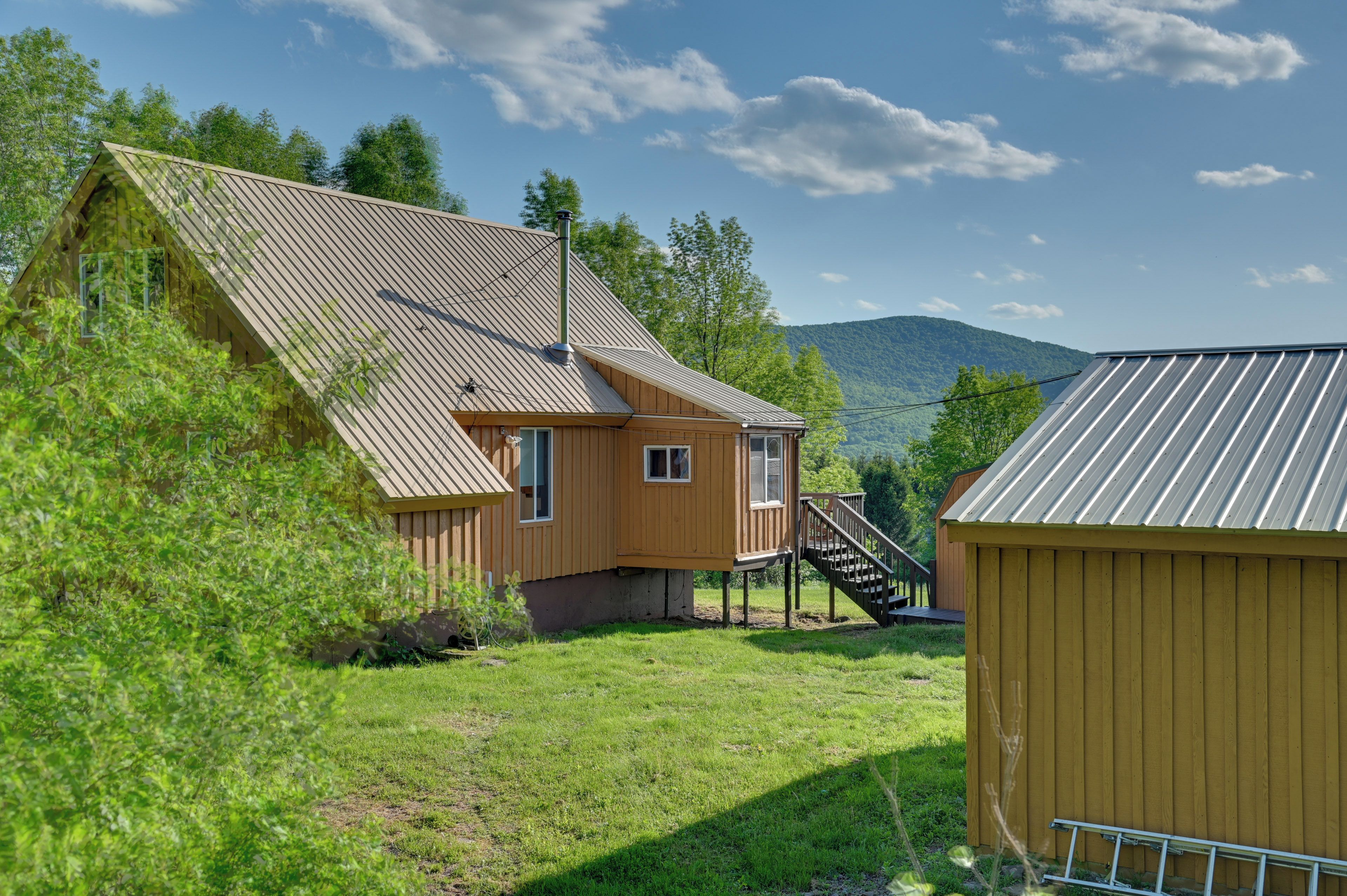 Een houten chalet met een schuin dak, een klein terras en een trap naar een dek.