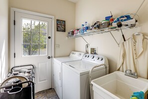 A laundry area with a washer and dryer, a drying rack, and a shelf with cleaning supplies.
