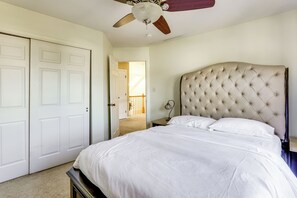 Ein Schlafzimmer mit einem geblümten Kopfstück, einem Bett mit weißen Leinentüchern, einem Deckenventilator und einer Tür zu einem anderen Raum.