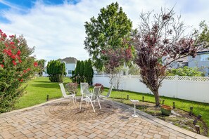 A patio area with a brick floor, white chairs, and a white fence in the background.