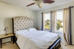 A bedroom with a tufted headboard, a bed with white linens, a bedside table with a lamp, and a window with curtains.